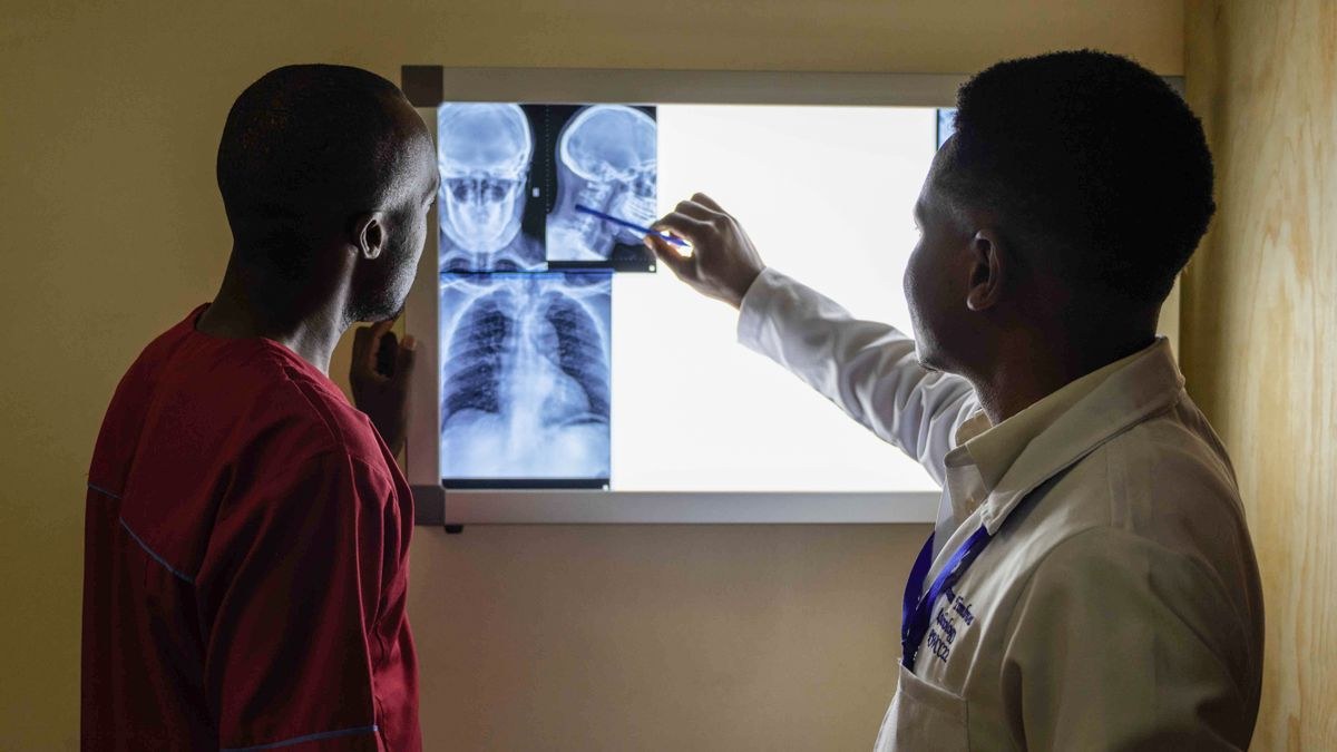 Doctor pointing at chest and skull X-rays on a lightbox while a patient stands beside him